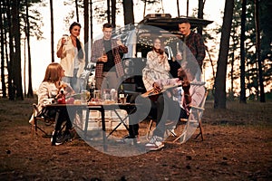 Evening time, by the table. Group of friends are together in the forest