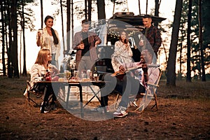 Evening time, by the table. Group of friends are together in the forest