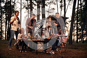 Evening time, by the table. Group of friends are together in the forest