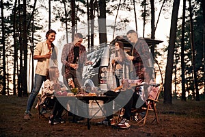 Evening time, by the table. Group of friends are together in the forest