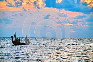 Evening tropical sea landscape with silhouette of a fishing boat with people.