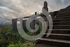 Evening view of an old abandoned wrecked house in the field overgrown with green ivy