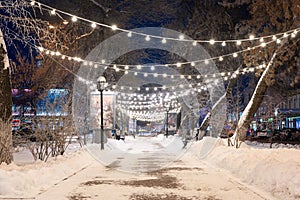 Evening winter alley with benches and New Year's decorations.