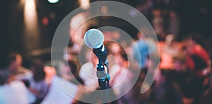 Event hall: Close up of microphone stand, seats with audience in the blurry background