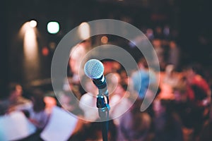 Event hall: Close up of microphone stand, seats with audience in the blurry background