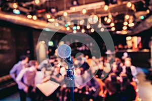 Event hall: Close up of microphone stand, seats with audience in the blurry background