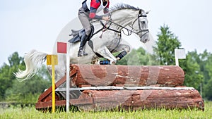 Eventing: equestrian rider jumping over an a log fence obstacle