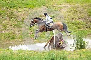 Eventing: equestrian rider jumping over an a log fence water obstacle