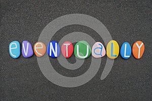 Eventually, adverb, creative text composed with multi colored stone letters over black sand photo