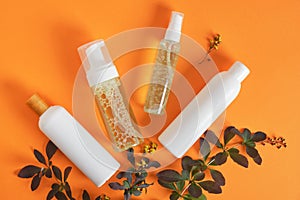 everal mock up cosmetic bottles and branch with leaves and flowers on orange background copy space top view flat lay