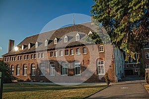 Evergreen garden with old brick building on blue sunset sky in Tielt.