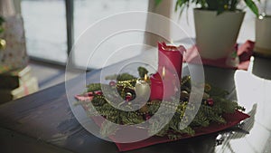 An evergreen wreath with two red candles and one golden candle. In the background, a decorated Christmas tree. Christmas