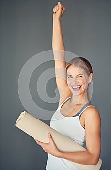 Every accomplishment starts with the decision to try. a woman expressing triumph while holding her yoga mat.