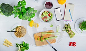 Every day healthy meal diet planning. Raw vegetables, fresh salad, notebook and phone on the white wooden table. Vegetarian and