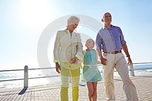 Every day is special with my grandparents. grandparents walking hand in hand with their granddaughter on a promanade.