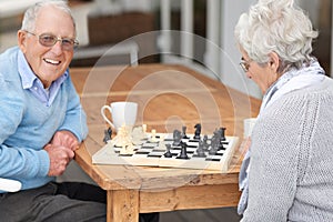 Every king needs a queen. An elderly couple playing chess together.