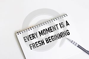 Every moment is a new beginning. Inspirational quote on notepad with pen