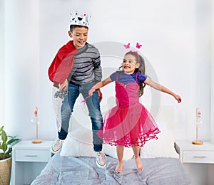 Every superhero learns how to fly eventually. two young children dressed up as superheroes jumping on a bed at home.