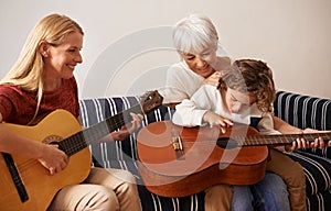 Everybody is jamming together. Shot of a little boy and his mother playing guitar with his grandmother sitting by.