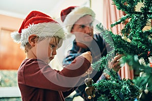 Everybodys favourite Christmas tradition. an adorable little boy decorating the Christmas tree with his father at home.