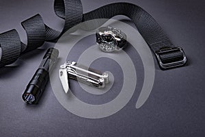 Everyday carry EDC items for men in black color - tactical belt, flashlight, watch and silver multi tool.