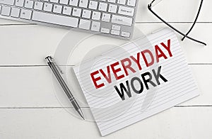 EVERYDAY WORK text on notebook with keyboard , pen glasses on white wooden background