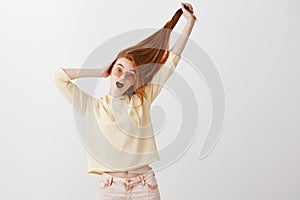 Everyone is jealous of her beautiful hair. Portrait of playful expressive young redhead in fashionable clothes and pink