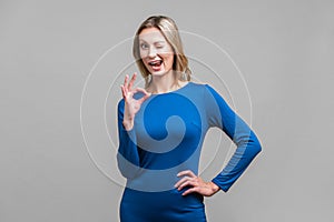 Everything is fine. Portrait of playful positive woman showing ok gesture. indoor studio shot isolated on gray background