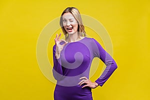 Everything is fine. Portrait of playful positive woman showing ok gesture. indoor studio shot isolated on yellow background