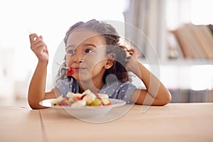 Everything good for a growing child. a cute little girl eating fruit salad at a table.