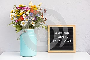 Everything happens for a reason. Motivational quote on letter board and bouquet colorful flowers on white table against