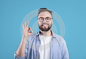 Everything is okay. Portrait of happy Caucasian guy showing OK gesture over blue studio background