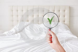 Everything in perfect and clean. Woman checks condition in hotel room, holds lens against white bed which demonstrates purity and