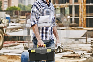 Everything what i need for work. Cropped image of a builder holding toolbox, protectives gloves and engineering drawings