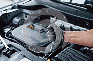 Everything will be fixed. Man`s hand in glove holds wrench in front of broken automobile