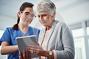 Everything you need is right here. a young female nurse and her senior patient looking at a tablet in the old age home.