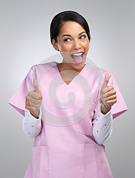 Everythings coming up trumps today. an attractive young female healthcare worker gesturing thumbs up in studio against a photo