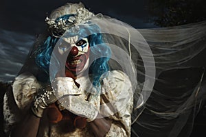 Evil clown in bride dress strangling a teddy bear photo