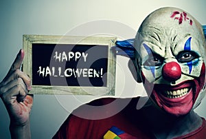 Evil clown with a chalkboard with the text happy Halloween