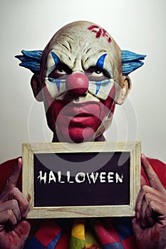 Evil clown with a chalkboard with the word Halloween