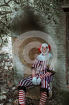 evil clown sitting in front of an old rustic house