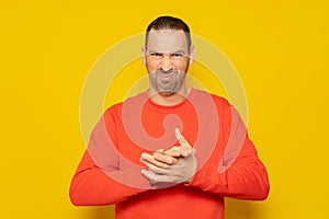 Evil hispanic man rubbing hands on isolated yellow background, person rubbing hands planning some kind of crime.