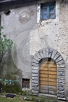 Evocative image, veiled by time, of the wall with stone arch and wooden door of an old house, in Vergemoli.