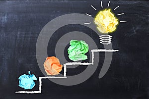 Evolving idea concept with colorful crumpled paper and light bulb on steps drawn on blackboard