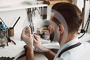 Exact size. Close up photo of a young male jeweler measuring ring with a tool in workshop.