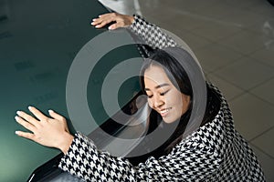 Exalted young asian woman hugging shining car hood photo