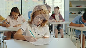 Exam in elementary school. Schoolboy wearing glasses sits at a first desk in the classroom and fills out tests, and the