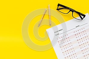 On the exam. Exam sheet, answer near glasses and pencil on yellow background top view space for text