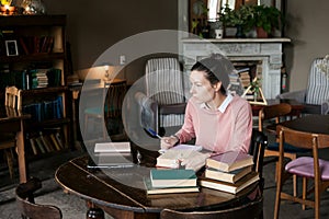 Exam preparation. Student girl in glasses and a pink sweater leaned over books, engaged in an old library at the table.