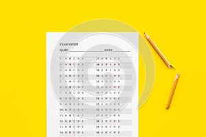 Exam sheet on yellow table flat lay space for text. Education concept